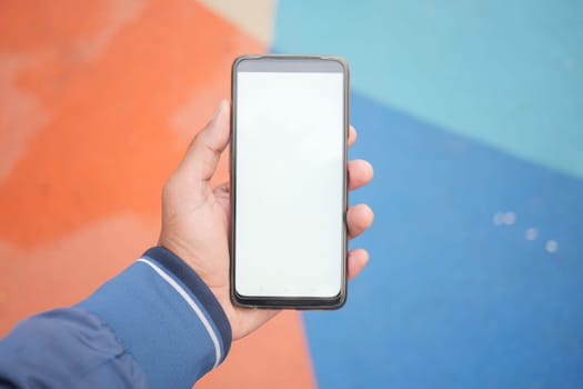 top view of hand holding a smart phone with empty screen on color background .