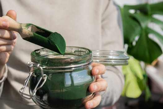 Female hands holding Organic blue-green algae spirulina detox powder in glass jar. Health protein of chlorella. Vitamins and minerals to diet. Prebiotic and antioxidant rich Dietary supplement Seaweed superfood concept