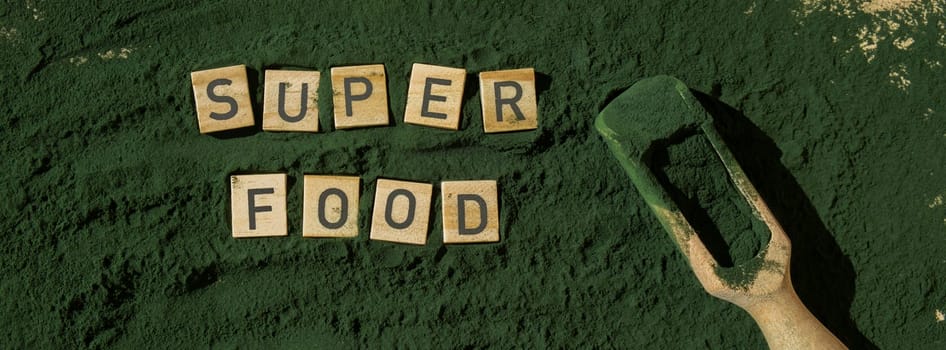 Wooden blocks with text SUPERFOOD chlorella on background of algae superfood powder. Healthy benefits supplement and vegan antioxidant healthy eating concept