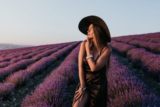 Close up portrait of young beautiful woman in a white dress and a hat is walking in the lavender field and smelling lavender bouquet.