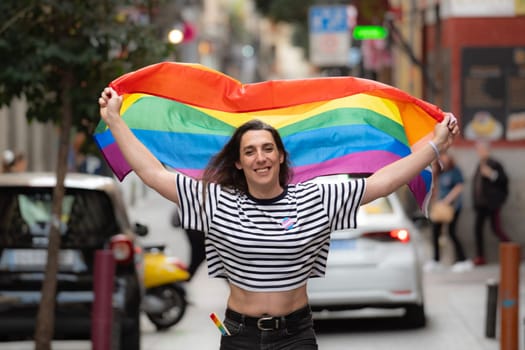 Portrait of a happy transgender girl waving a rainbow flag in a city street. LGBTQ community and diversity concept.