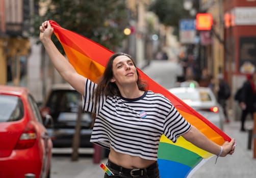 A transgender woman holding a rainbow flag in a city street. The flag is a symbol of the LGBTQ community.