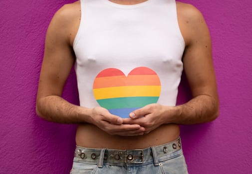 Unrecognizable homosexual man holding a rainbow heart in his hands isolated on purple background.