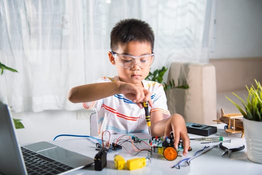 Asian kid boy assembling the Arduino robot car homework project at home, Little child tighten the nut with a screwdriver to assemble car toy, creating electronic AI technology workshop school lesson