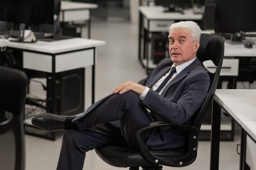 Portrait of a pensive mature business man sitting in a chair in the office. Vertical photo