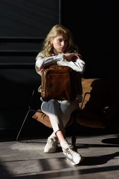 A woman holds leather backpack. Model wearing stylish knitted vest, white shirt and classic trousers.