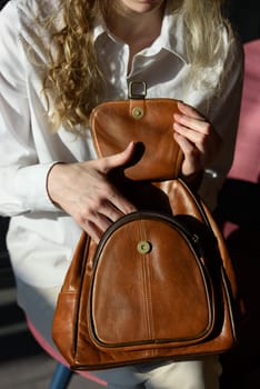 A woman holds leather backpack. Model wearing stylish knitted vest, white shirt and classic trousers.