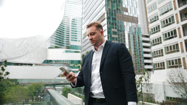 Caucasian business man hold mobile phone and looking at skyscraper view. Skilled male leader standing rooftop in modern building. Caucasian executive manager look at phone while rest his eyes. Urbane.