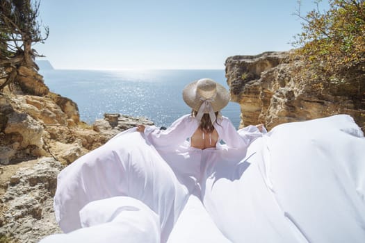 A woman in a white dress is standing on a rocky beach with her hat on. The scene is serene and peaceful, with the woman enjoying the view of the water.