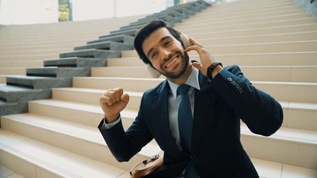 Closeup image of professional business man enjoy to listen music by using headphone. Portrait of skilled project manager show facial expression about joy and happy while sitting at mall. Exultant.