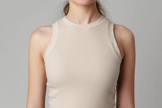 Female body in beige top on gray background close up