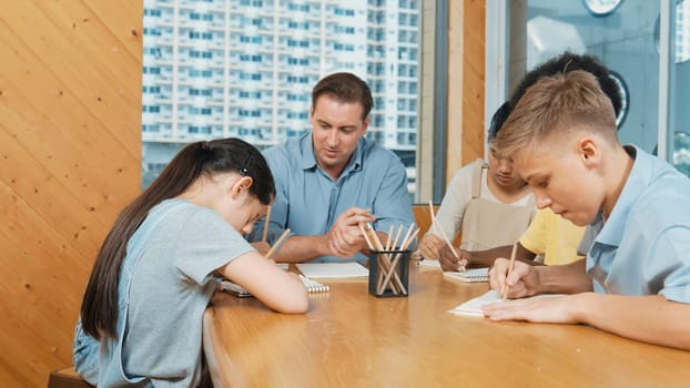 Smart highschool boy in casual shirt asking professional teacher while student with mixed races writing book. Caucasian instructor giving comment while creative child pointing at note. Edification.