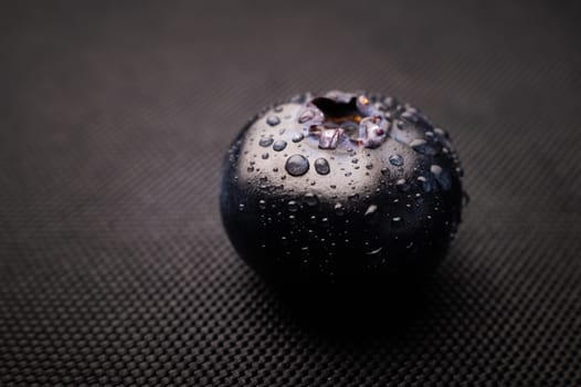 One blueberry covered with water drops on black background. Very detailed macro shoot with copy space.