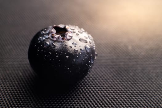 One blueberry covered with water drops on black background. Very detailed macro shoot with copy space.