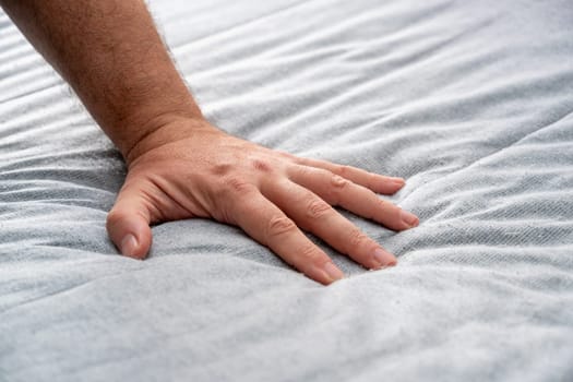 The man checks the quality and softness of the new mattress he will buy by pressing it with his hand