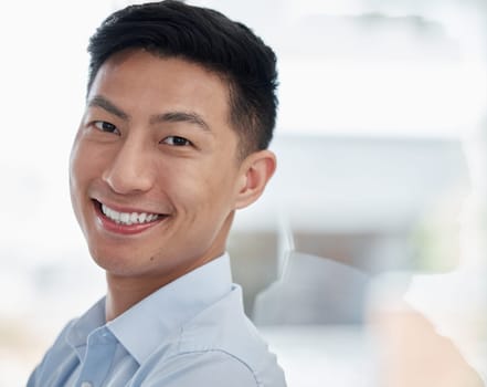 Asian man, portrait and business with smile for career ambition, entrepreneur or creative mindset at modern office. Face of young businessman leaning on glass wall in confidence for job or reflection.