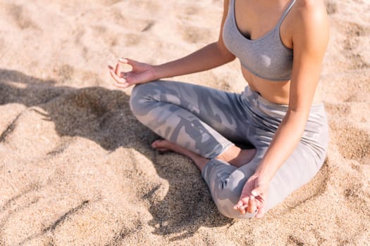 detail of the crossed legs and torso of an unrecognizable woman doing meditation sitting on the beach sand, concept of mental relaxation and healthy lifestyle