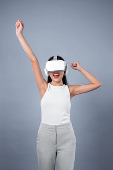 Smart female standing with gray background wearing VR headset connecting metaverse, futuristic cyberspace community technology. Elegant woman excited seeing generated virtual scenery. Hallucination.