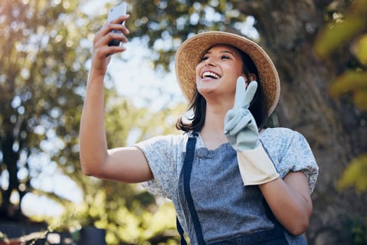 Happy, woman and florist taking selfie with peace sign on mobile for social media, networking outdoor in nature at nursery. Female person and smile with smartphone and hand gesture for connection.