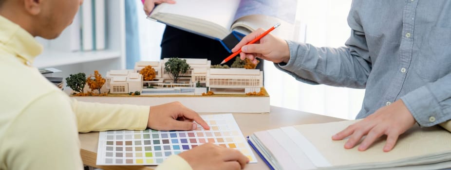 Cropped image of professional interior design team discuss about color and material usage for the project while project manager choose main theme color with house model on meeting table. Variegated.