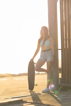A woman is standing on a sidewalk holding a skateboard. She is wearing a white bikini top and shorts