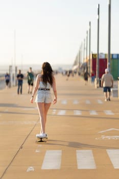 A woman is skateboarding down a sidewalk. There are several other people walking around her. The scene is lively and bustling, with people going about their day