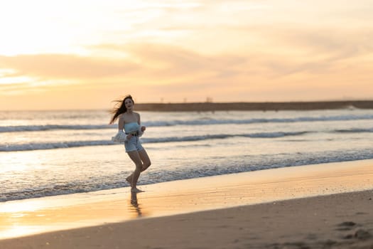 A woman is running on the beach at sunset. The sky is orange and the water is calm