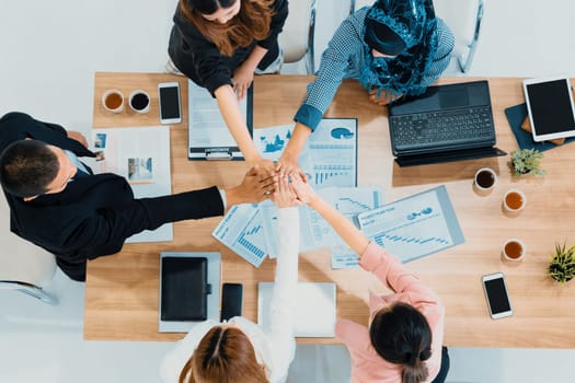 Businessmen and businesswomen joining hands in group meeting at multicultural office room showing teamwork, support and unity in business. Diversity workplace and corporate people working concept. uds