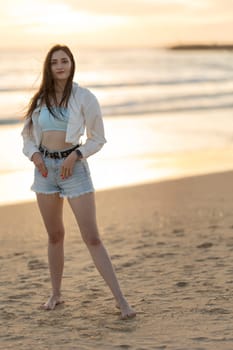 A woman is standing on the beach wearing a white shirt and blue shorts. She is posing for a picture