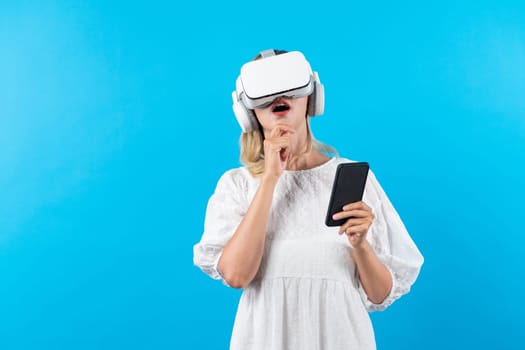 Caucasian girl wearing VR glasses while holding phone and pointing at view. Happy woman surprised while looking around to explore visual reality world or metaverse. Technology innovation. Contraption.