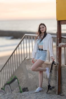 A woman is standing on a concrete ledge with a skateboard in her hand. She is wearing a white shirt and blue shorts. The image has a casual and relaxed vibe