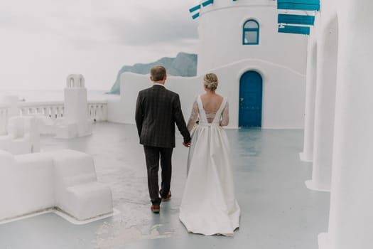 A bride and groom are walking down a path in front of a blue door. The bride is wearing a white dress and the groom is wearing a suit. Scene is romantic and happy