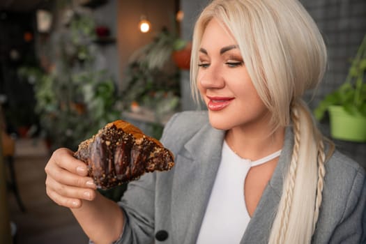 A blonde woman is eating a chocolate pastry. She is smiling and she is enjoying her treat