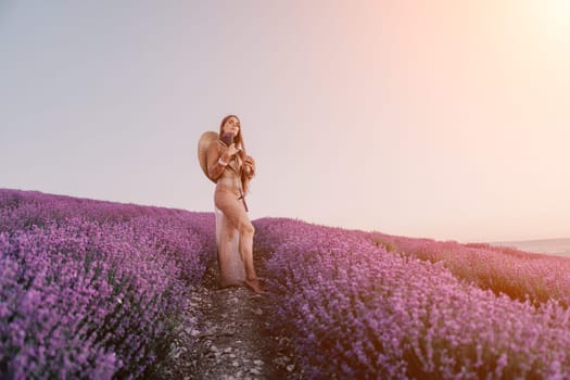 Close up portrait of young beautiful woman in a white dress and a hat is walking in the lavender field and smelling lavender bouquet.