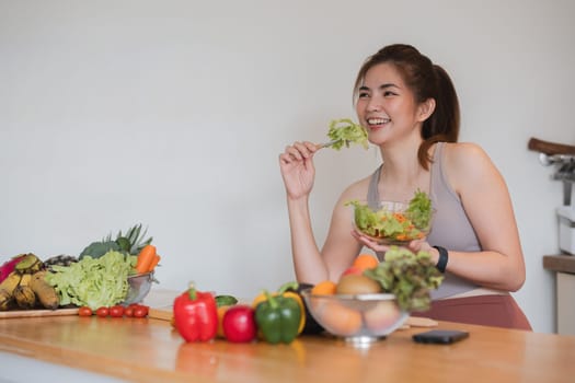 A woman is eating a salad in front of a table full of fruits and vegetables. She is smiling and she is enjoying her meal