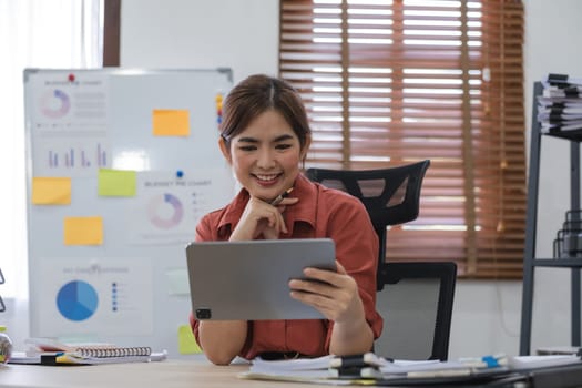 Portrait of Young Asian woman hand freelancer is working her job on computer tablet in modern office. Doing accounting analysis report real estate investment data, Financial and tax systems concept..