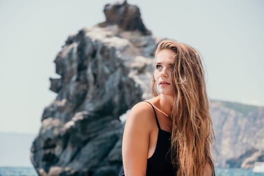 Woman travel sea. Young Happy woman in a long red dress posing on a beach near the sea on background of volcanic rocks, like in Iceland, sharing travel adventure journey