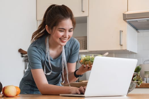 A woman is smiling while holding a laptop and a bowl of salad. She is wearing a blue shirt and a blue headband