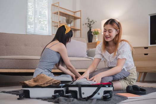 Two women are sitting on the floor in front of a suitcase, one of them is folding a pillow. Scene is lighthearted and playful