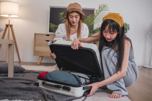 Two women are opening a suitcase in a living room. One of them is wearing a yellow hat