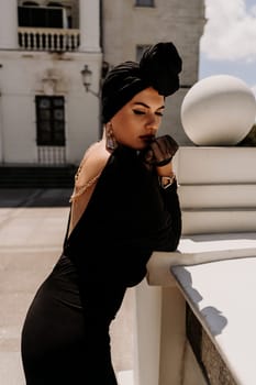 Stylish woman in the city. Fashion photo of a beautiful model in an elegant black dress posing against the backdrop of a building on a city street.