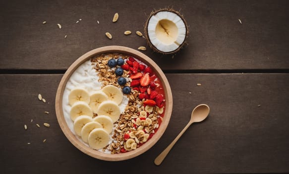 Colorful smoothie bowl in a coconut shell, topped with banana, goji berries, granola, and coconut flakes.