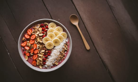 Colorful smoothie bowl in a coconut shell, topped with banana, goji berries, granola, and coconut flakes.