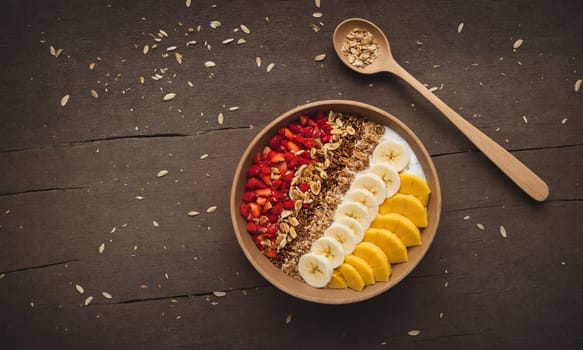 Colorful smoothie bowl in a coconut shell, topped with banana, goji berries, granola, and coconut flakes.