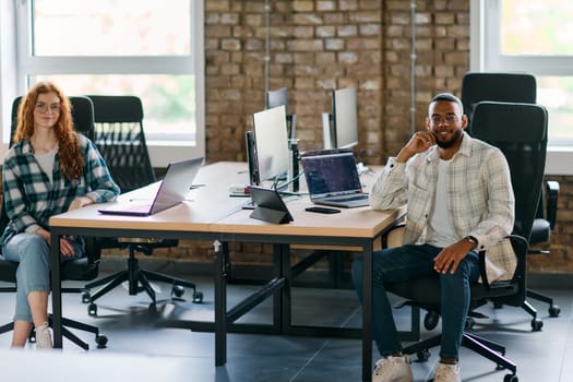 Group of colleagues, a woman with vibrant orange hair and a young African American businessman, sitting in a modern office space, symbolizing diverse collaboration and a dynamic work environment