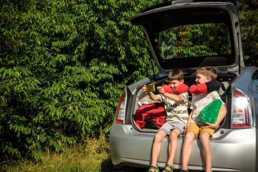 Two adorable little kids boy sitting in car trunk just before leaving for summer vacation. Sibling brothers making selfie on smartphone. Happy family going on long journey.