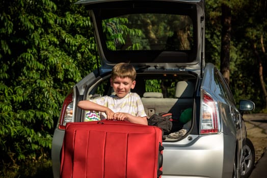 Pretty boy loading the luggage in the trunk of the car. Kid looking forward for a road trip or travel. Family travel by car.