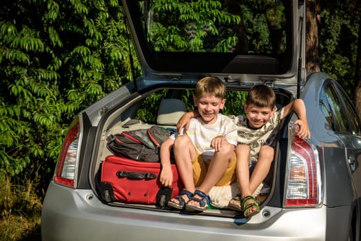 Two cute boys sitting in a car trunk before going on vacations with their parents. Two kids looking forward for a road trip or travel. Summer break at school. Family travel by car.