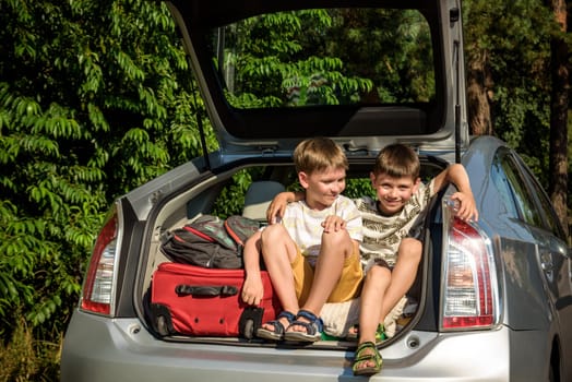 Two cute boys sitting in a car trunk before going on vacations with their parents. Two kids looking forward for a road trip or travel. Summer break at school. Family travel by car.