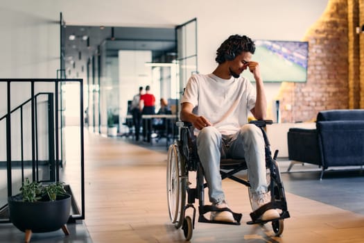 A African-American teenager in a wheelchair sits sadly amidst the bustling backdrop of a modern startup office, surrounded by his business colleagues